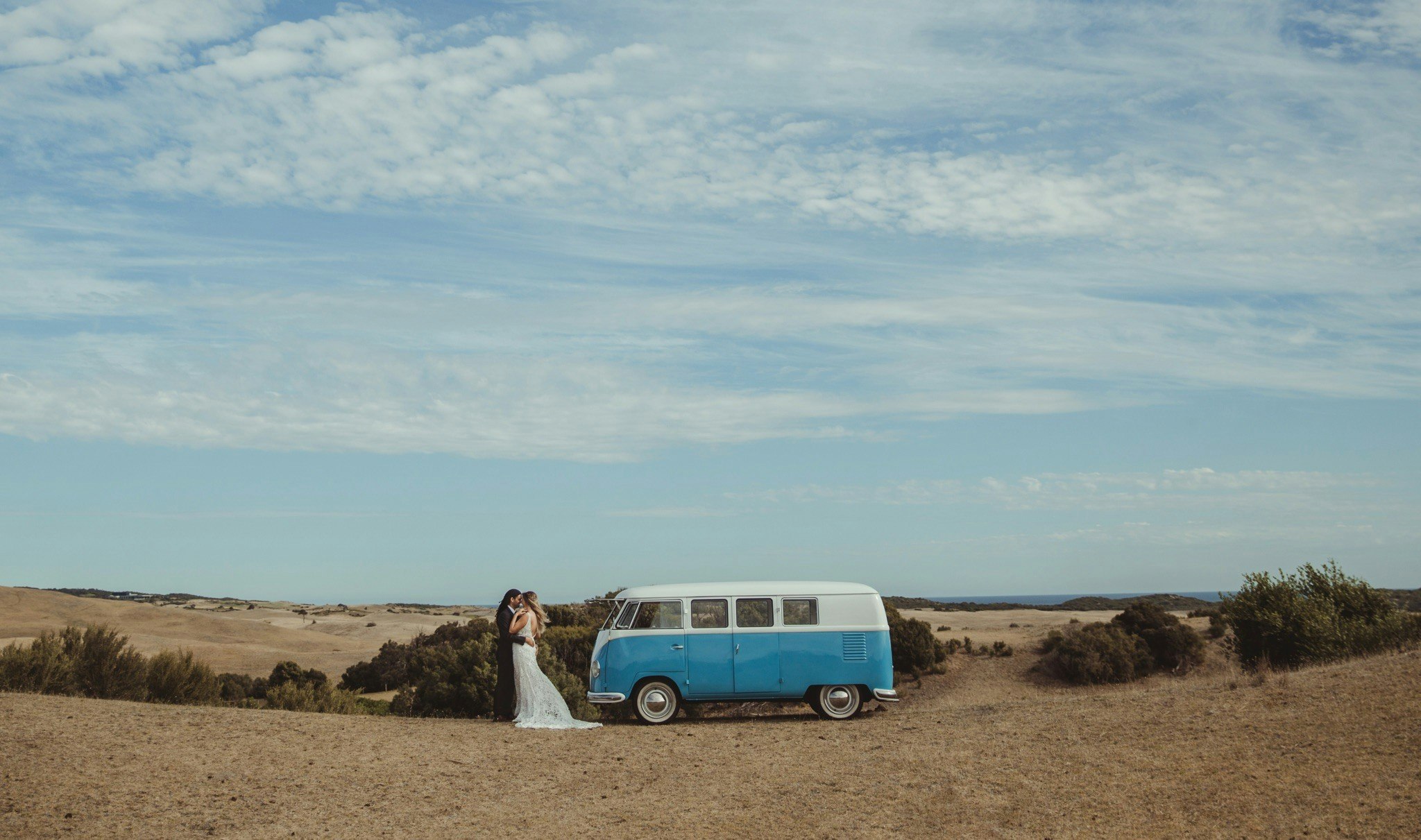Wedding couple hug beside a VW Kombi outdoors.
